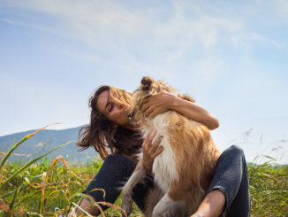 Eine junge Frau umarmt ihren Collie mitten auf einer grünen Wiese